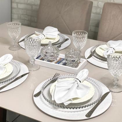 Mesa posta com sousplats brancos, louças de vidro com borda pérola e taças de cristal