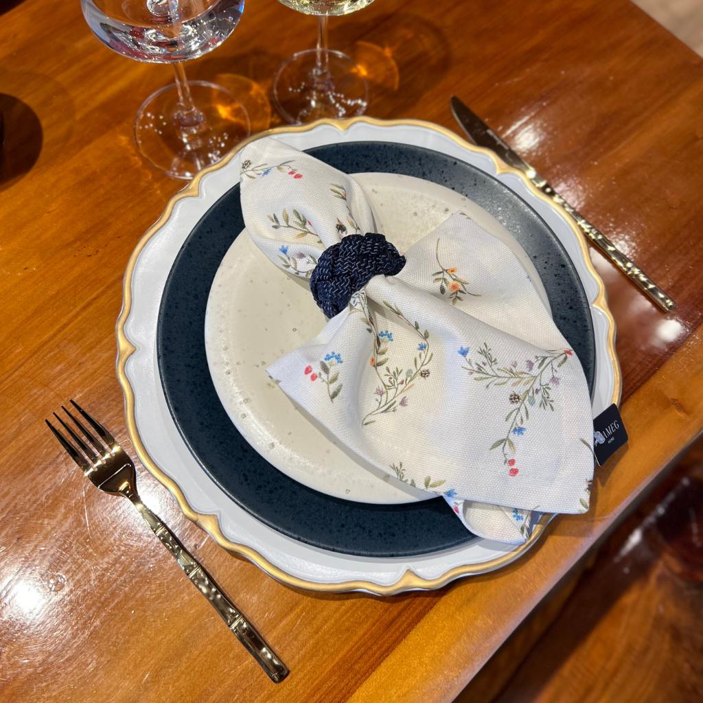 Sousplat elegante com borda dourada, louça e guardanapo floral em mesa de madeira