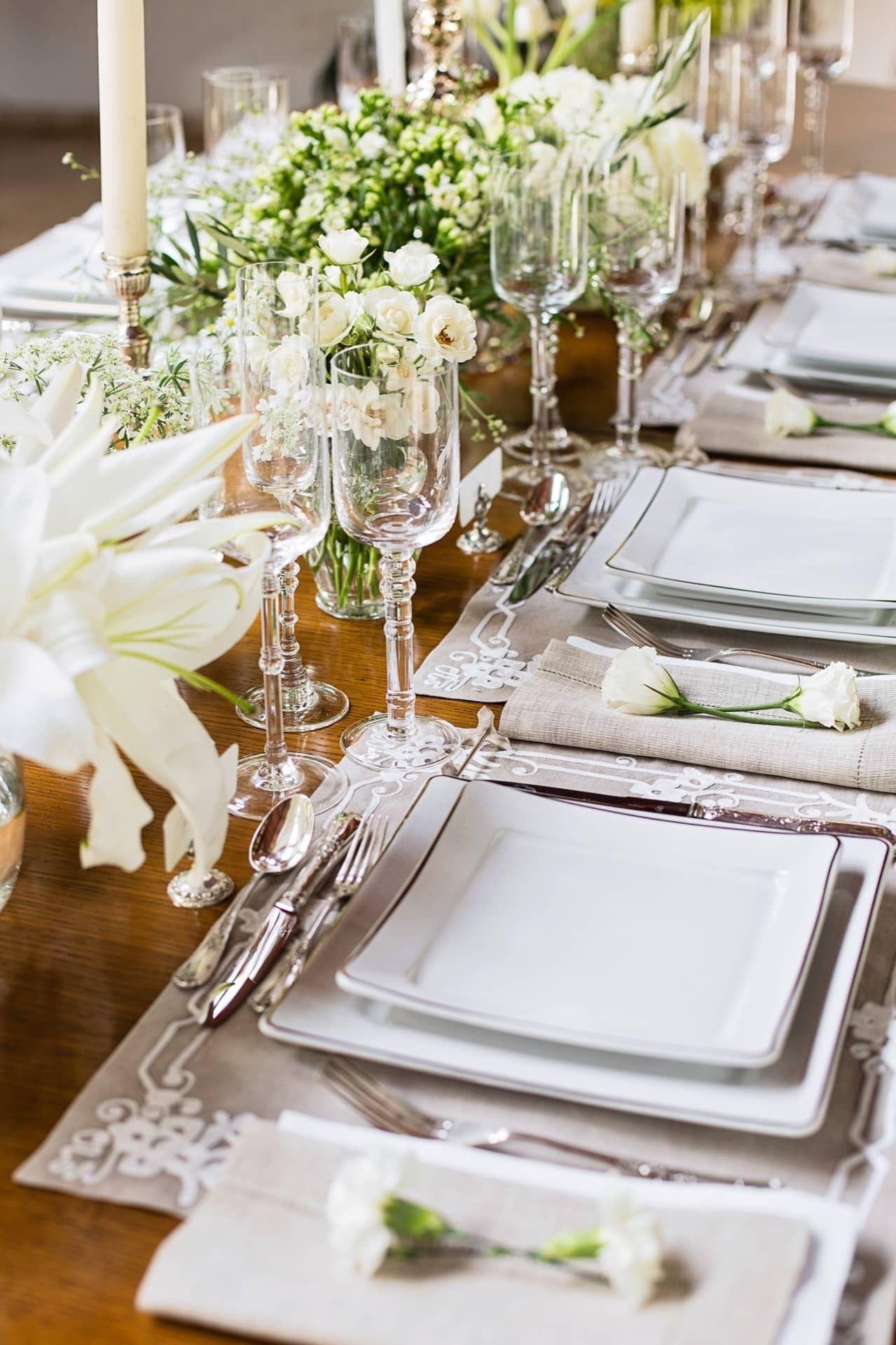 Mesa posta elegante com sousplats, louças brancas, flores e velas em ambiente sofisticado
